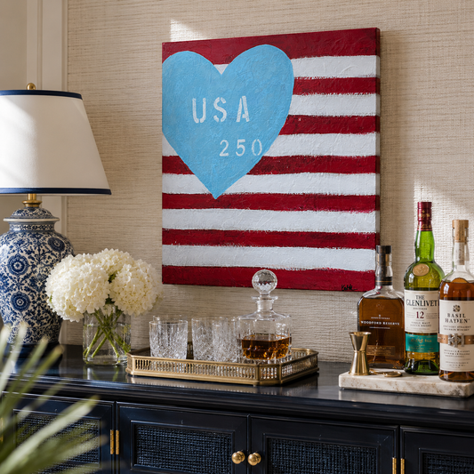 Decorative shelf with a 'USA 250' heart-themed painting, bottles, and glasses.
