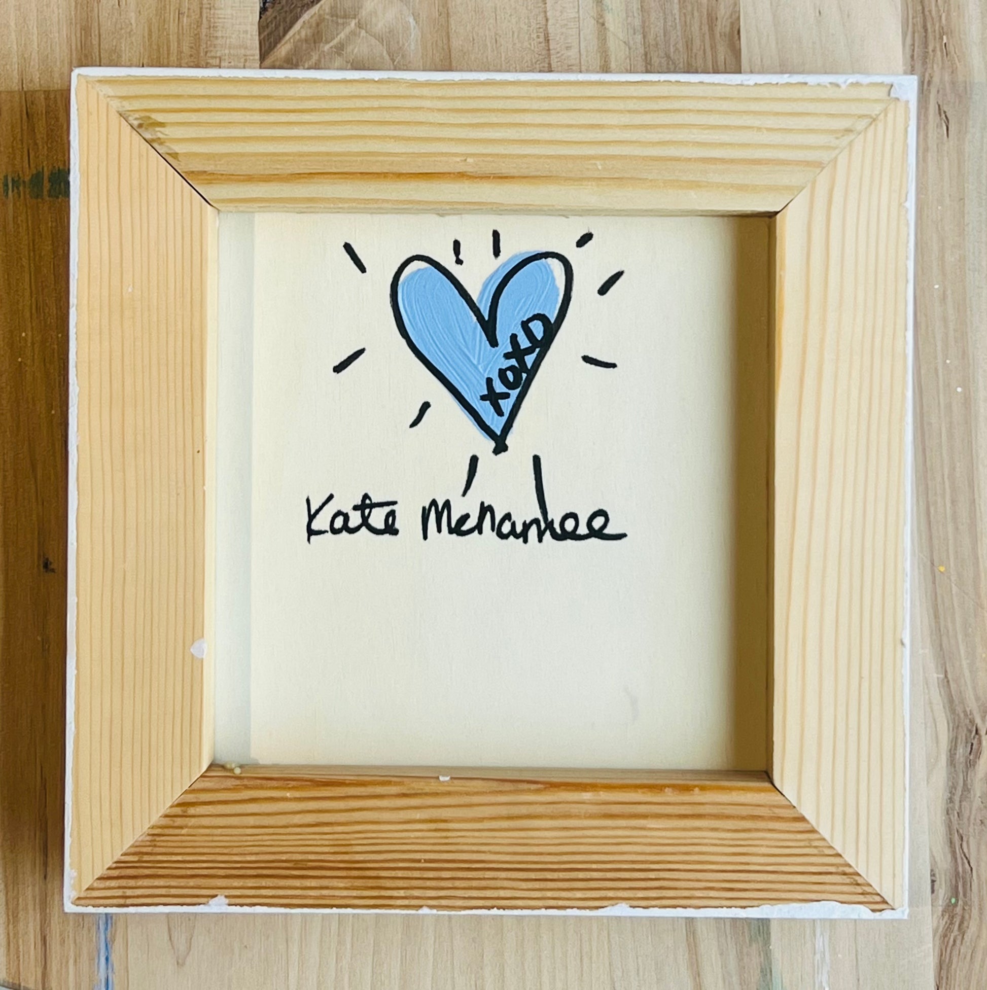 Small framed artwork with a blue heart and text on a wooden surface
