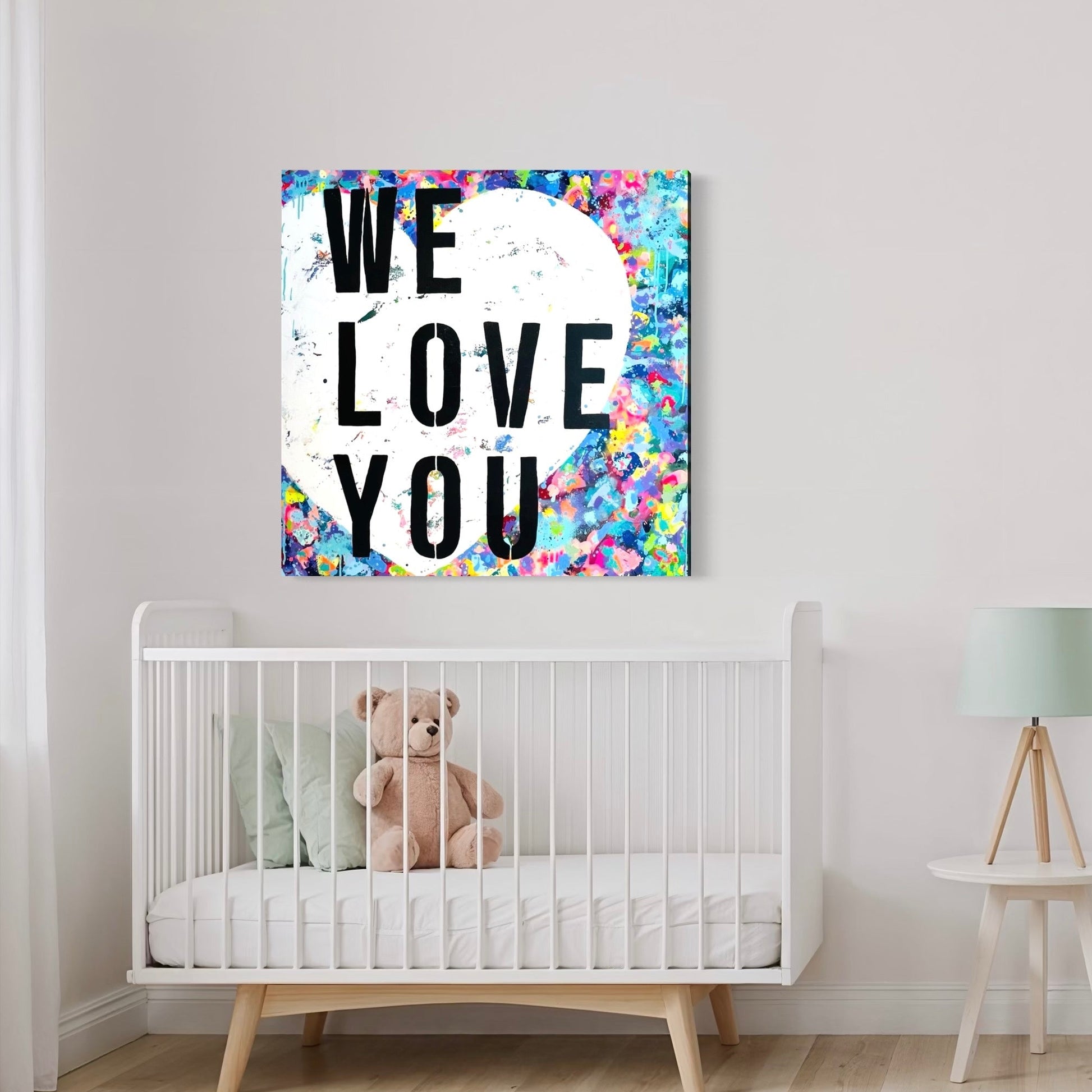 Nursery room with a crib, teddy bear, and colorful 'WE LOVE YOU' wall art.