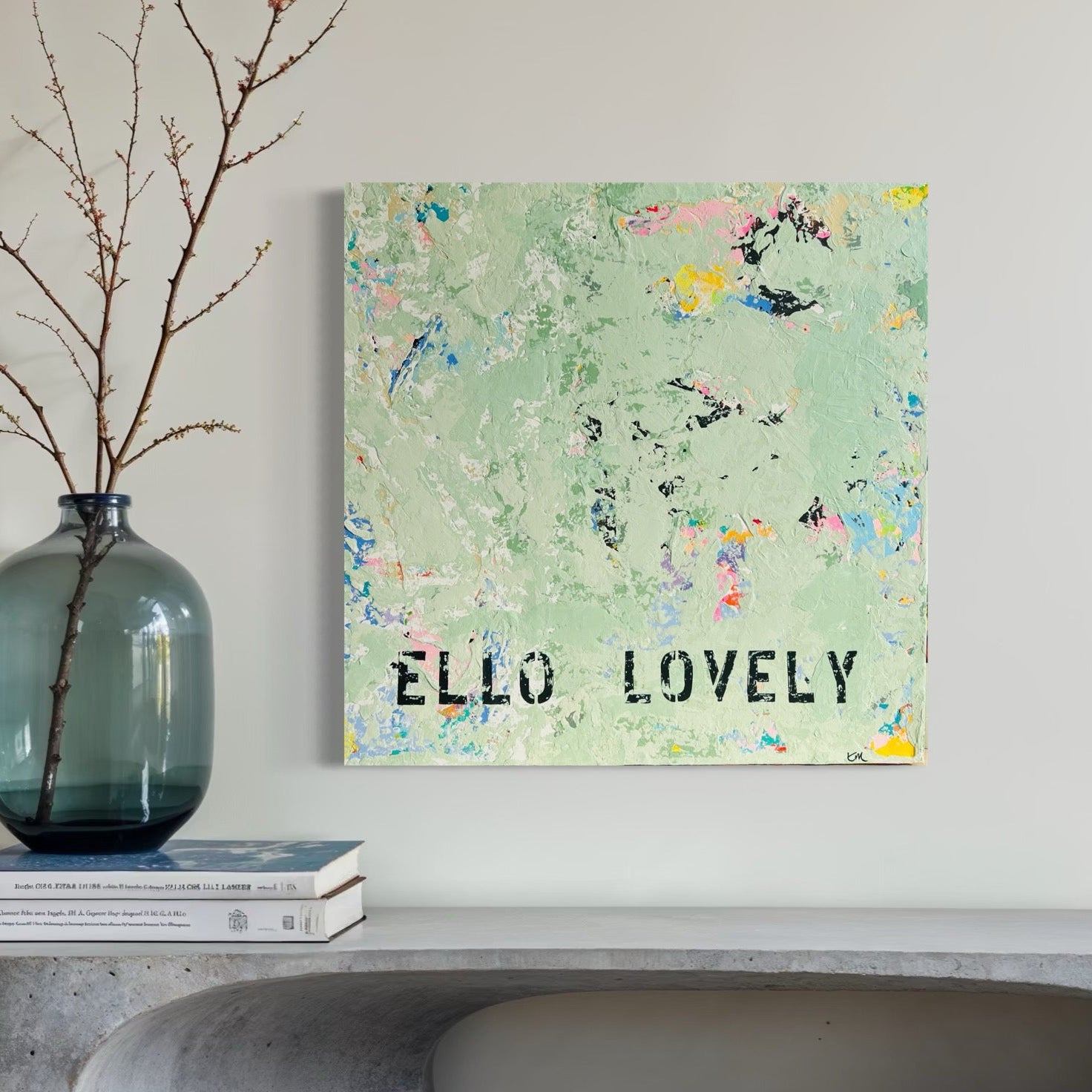 Decorative wall art with 'ELLO LOVELY' text on a light background, displayed above a concrete console table.