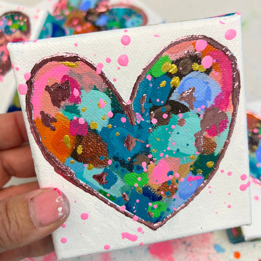 Small square canvas with a colorful heart design held by a hand.