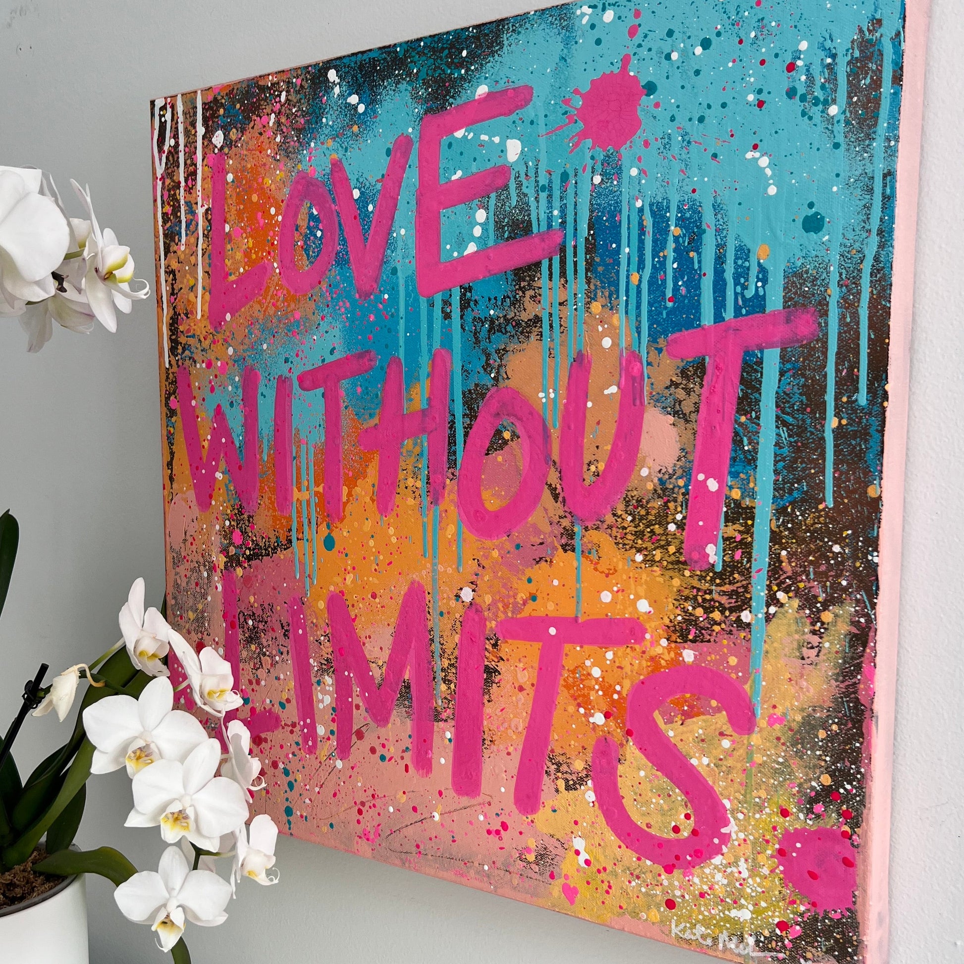 Colorful abstract painting with 'Love Without Limits' text on a white wall, accompanied by a plant.